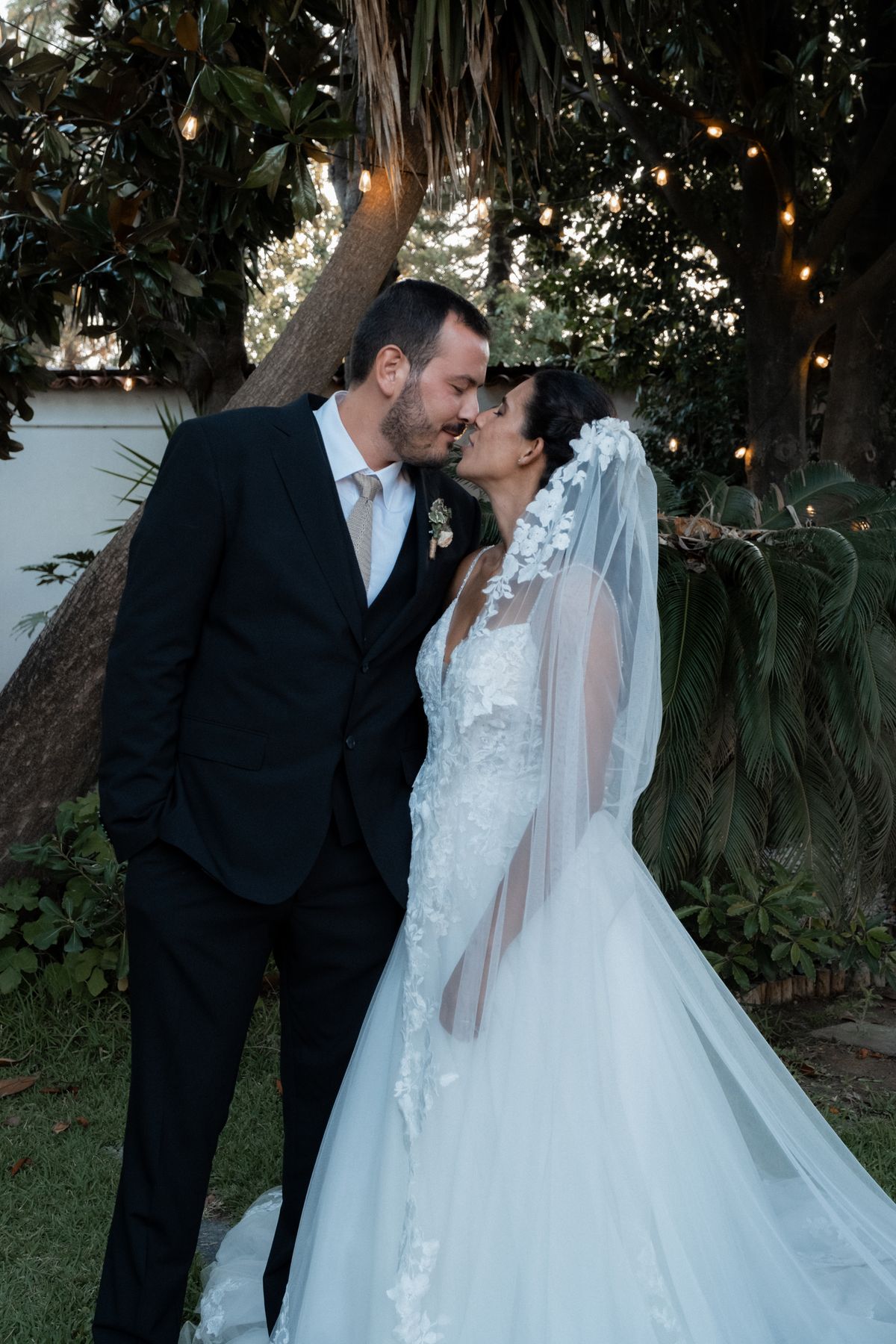 Noivos a beijar-se num jardim com luzes suspensas
